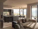 INTERIOS. Dein Interior-Design-Studio. Modernes Wohnzimmer mit Küche, Sofa und Panoramafenstern mit Blick auf Landschaft und Meer