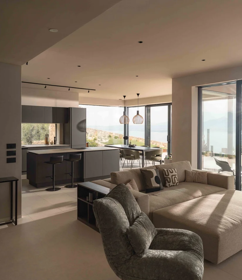 INTERIOS. Dein Interior-Design-Studio. Modernes Wohnzimmer mit Küche, Sofa und Panoramafenstern mit Blick auf Landschaft und Meer