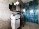 INTERIOS. Dein Interior-Design-Studio. Moderner Badbereich mit weißem Waschbecken und blauen Fliesen in der Dusche