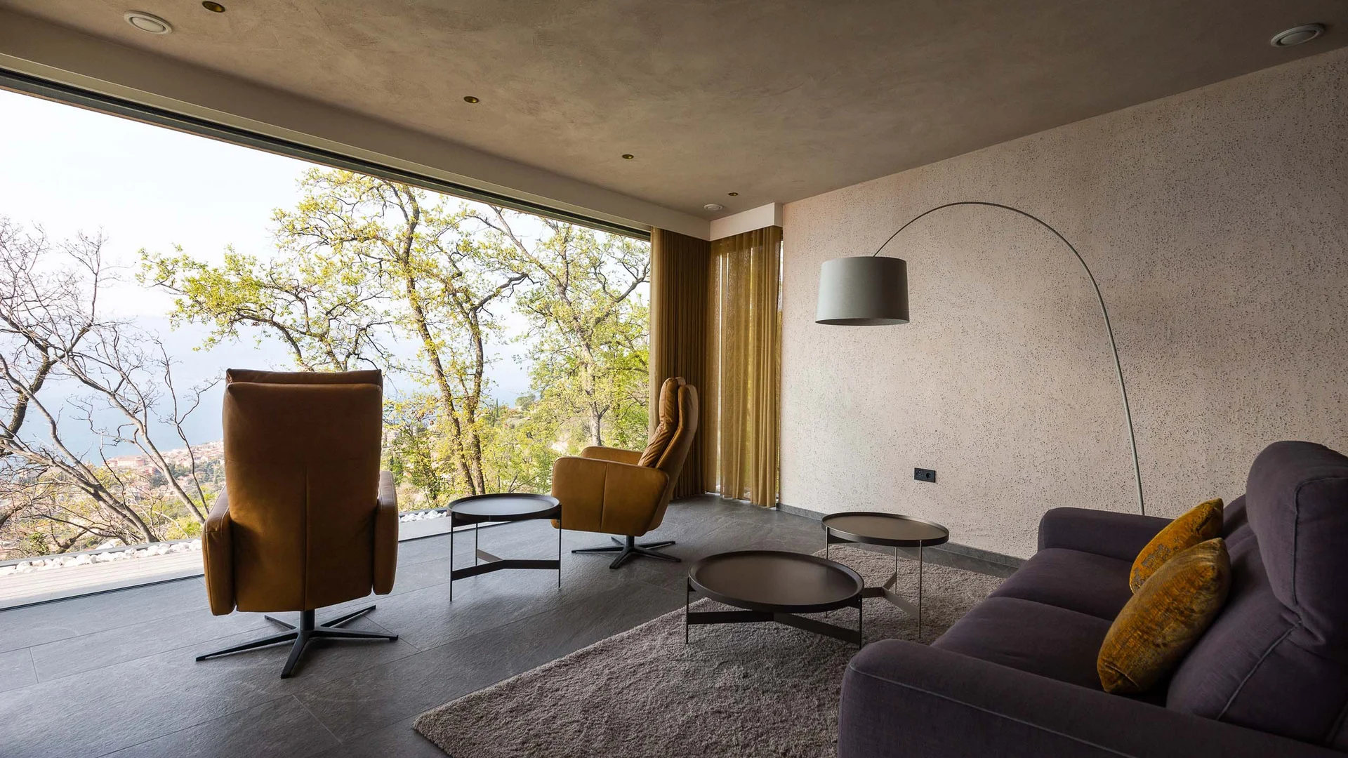 INTERIOS. Dein Interior-Design-Studio. Modernes Wohnzimmer mit großen Fenstern und Blick auf Bäume und Landschaft