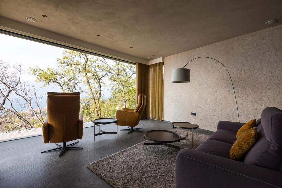 INTERIOS. Dein Interior-Design-Studio. Modernes Wohnzimmer mit großen Fenstern und Blick auf Bäume und Landschaft