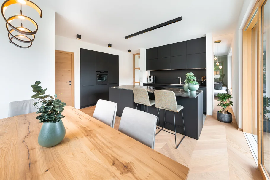 INTERIOS. Dein Interior-Design-Studio. Moderne schwarze Küche mit Holz-Esstisch und großer Fensterfront