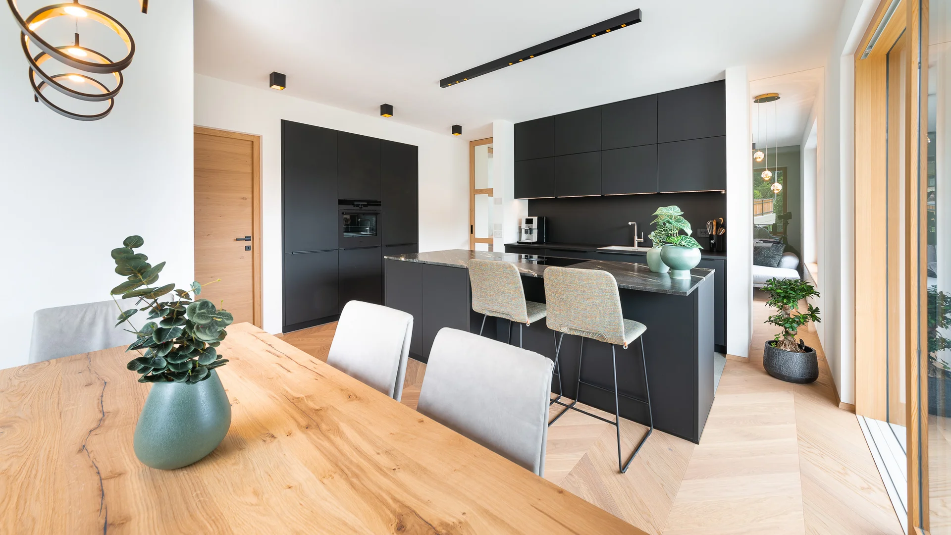 INTERIOS. Dein Interior-Design-Studio. Moderne schwarze Küche mit Holz-Esstisch und großer Fensterfront