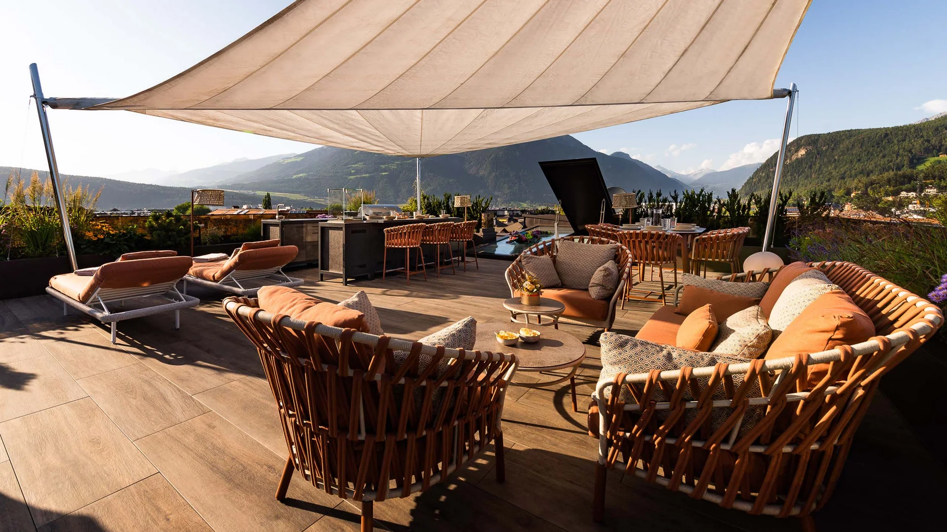 INTERIOS. Dein Interior-Design-Studio. Sonnenterrasse mit Korbmöbeln und Bergblick bei klarem Himmel