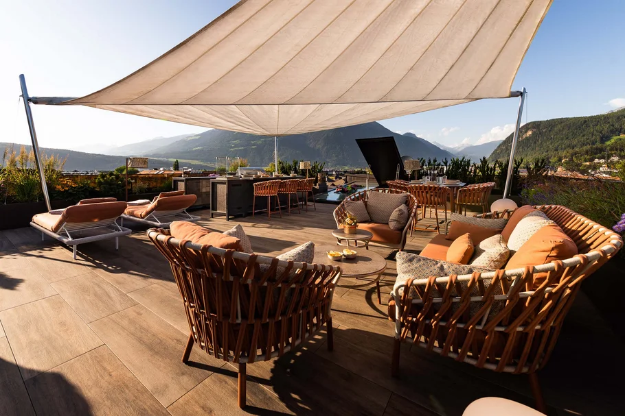 INTERIOS. Dein Interior-Design-Studio. Sonnenterrasse mit Korbmöbeln und Bergblick bei klarem Himmel