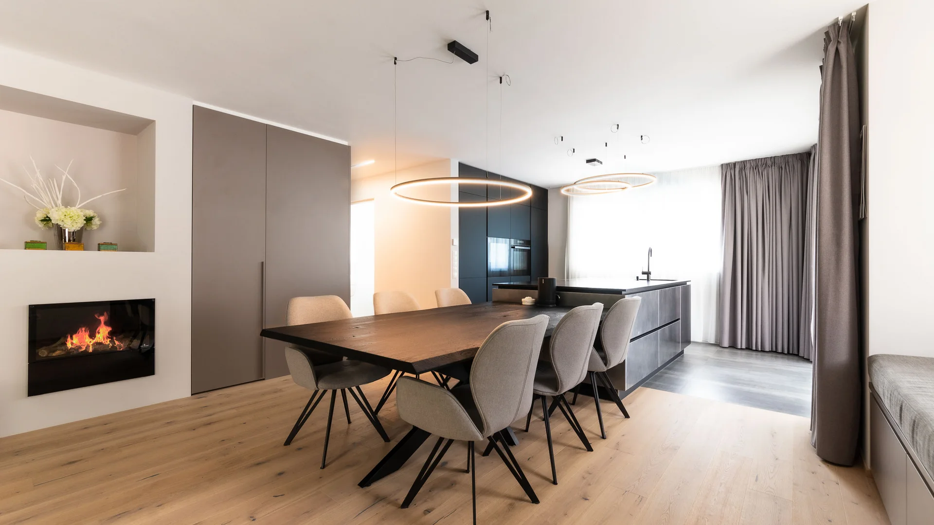 INTERIOS. Dein Interior-Design-Studio. Moderner Essbereich mit großem Holztisch, sechs Stühlen und integriertem Kamin