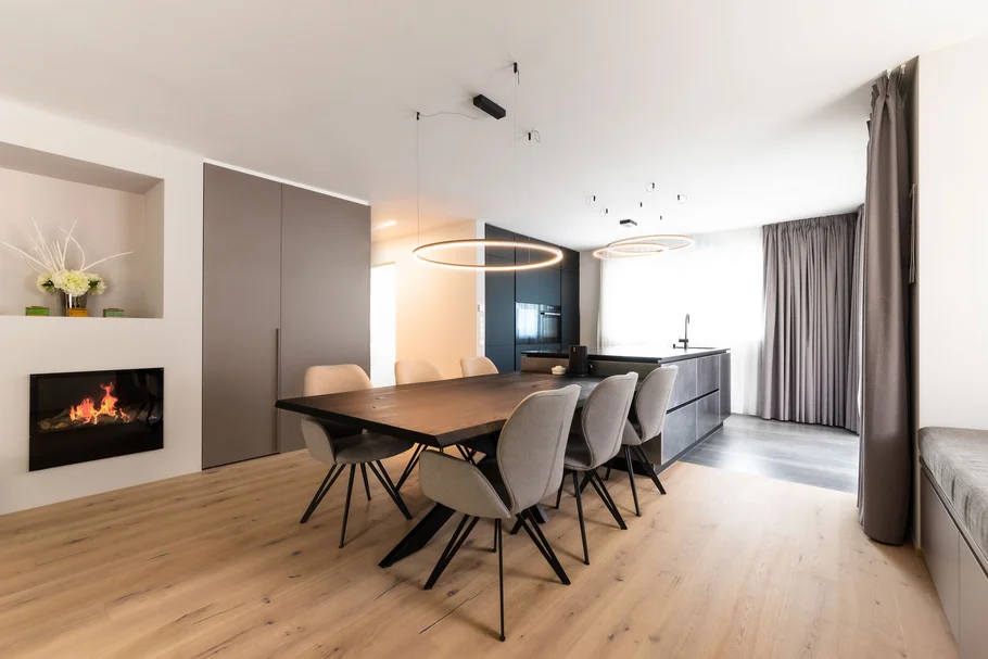 INTERIOS. Dein Interior-Design-Studio. Moderner Essbereich mit großem Holztisch, sechs Stühlen und integriertem Kamin