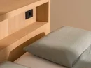INTERIOS. Dein Interior-Design-Studio. Bett mit hellgrüner Bettwäsche, Kissen und hölzernem Kopfteil mit Ablagefach