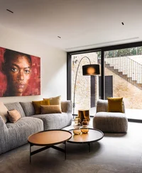 INTERIOS. Dein Interior-Design-Studio. Modernes Wohnzimmer mit hellgrauem Sofa, Pölstern und großer Fensterfront mit Treppe außen