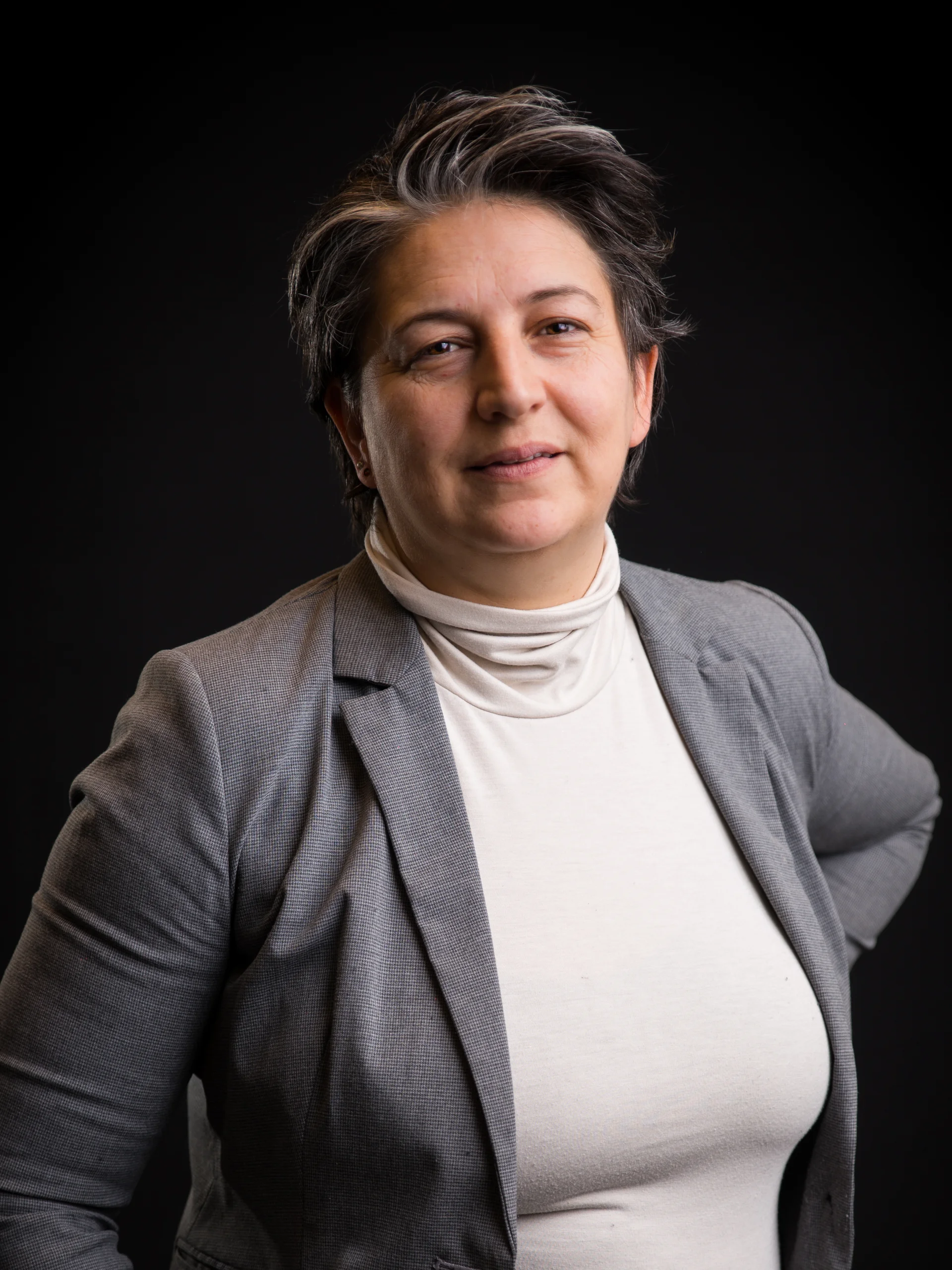 INTERIOS. Dein Interior-Design-Studio. Portrait einer Person in grauem Blazer vor schwarzem Hintergrund