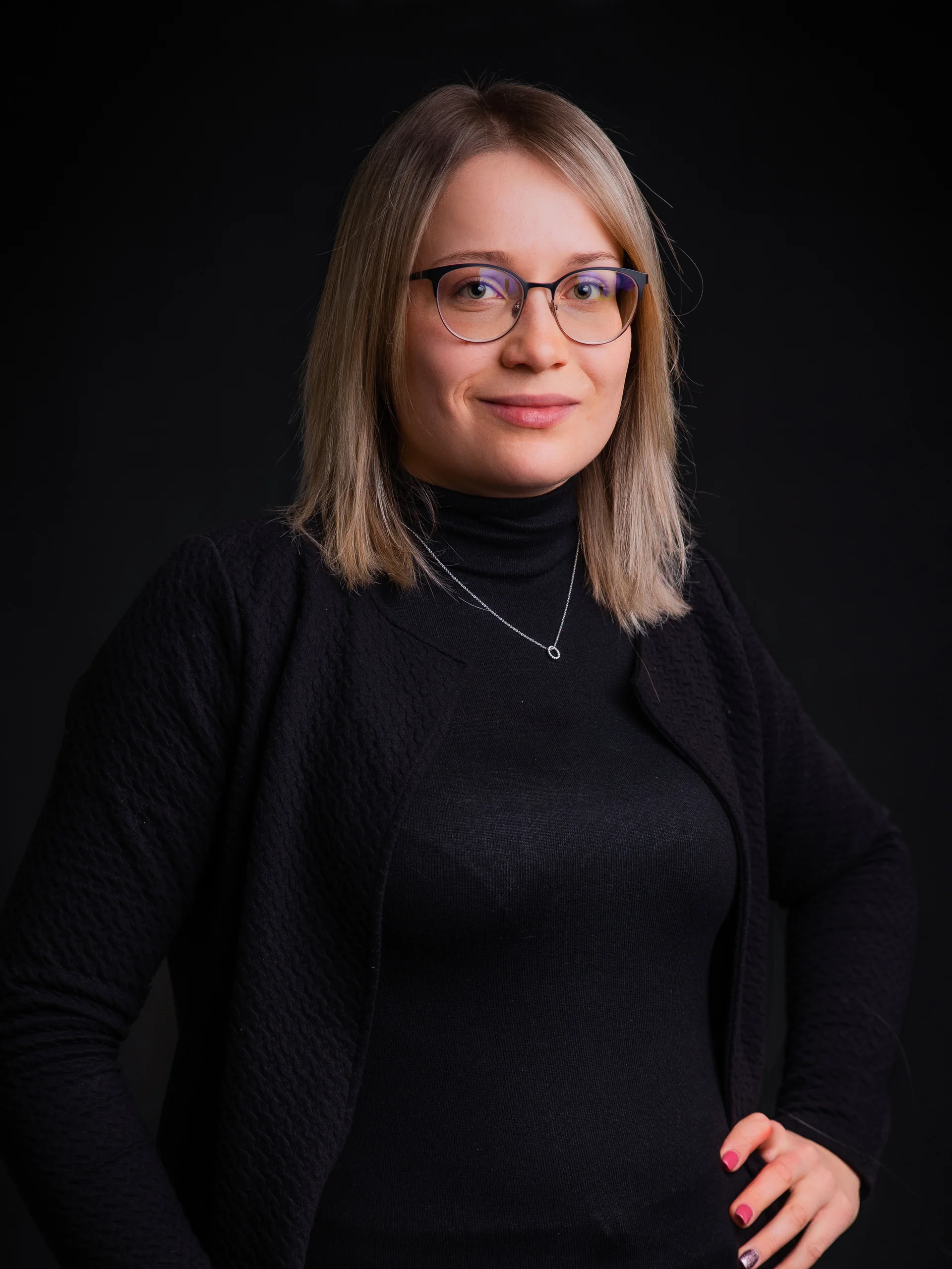 INTERIOS. Dein Interior-Design-Studio. Porträt einer Frau mit Brille und schwarzem Pullover vor schwarzem Hintergrund