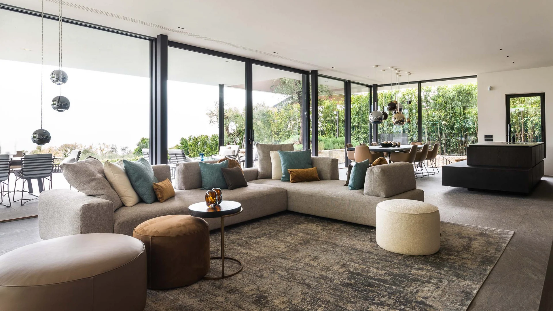 INTERIOS. Dein Interior-Design-Studio. Moderner Wohnbereich mit Ecksofa, Sitzhockern und großen Glasfenstern