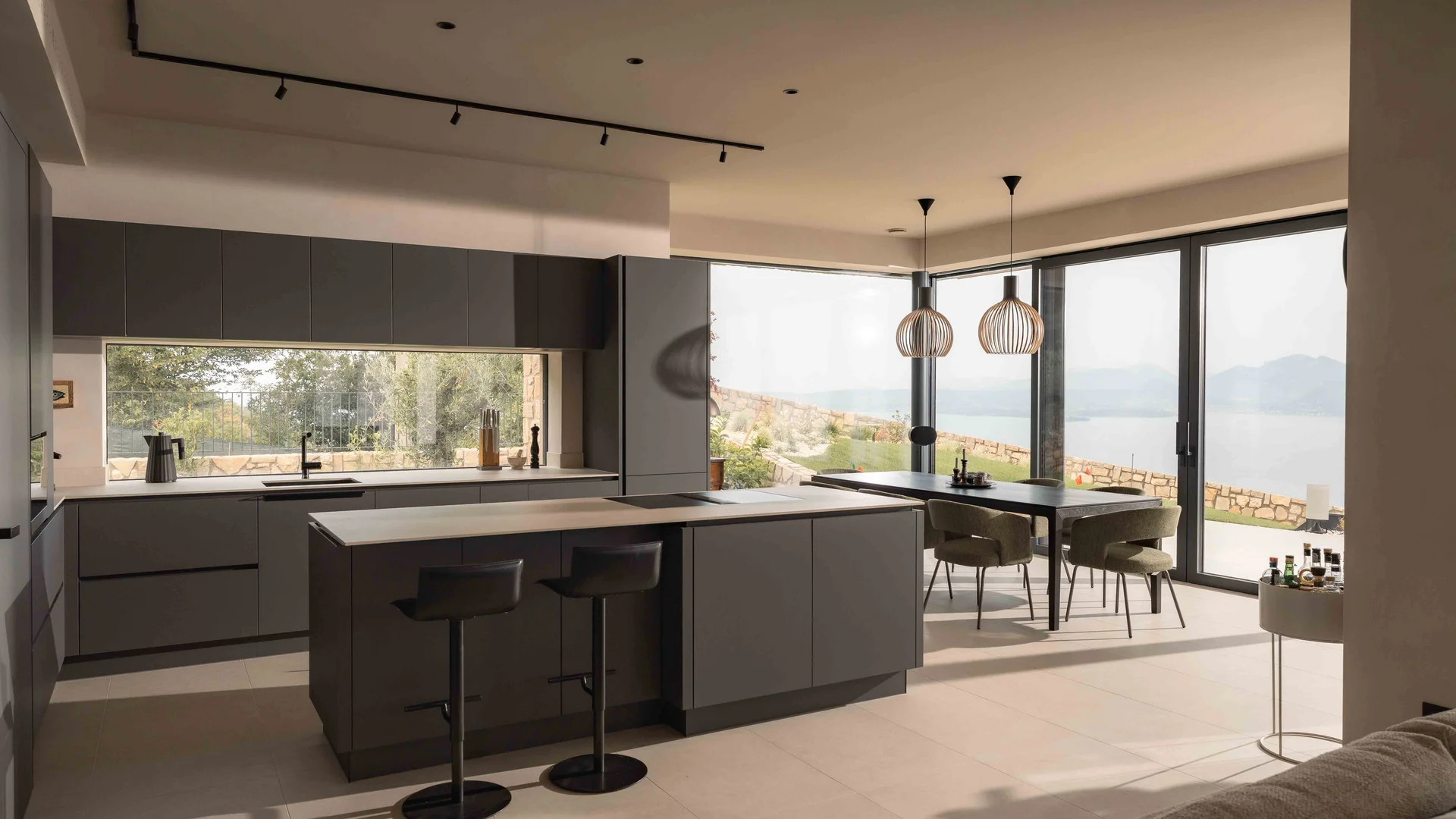 INTERIOS. Dein Interior-Design-Studio. Moderne Küche mit Kochinsel, Essbereich und Seeblick durch große Fenster