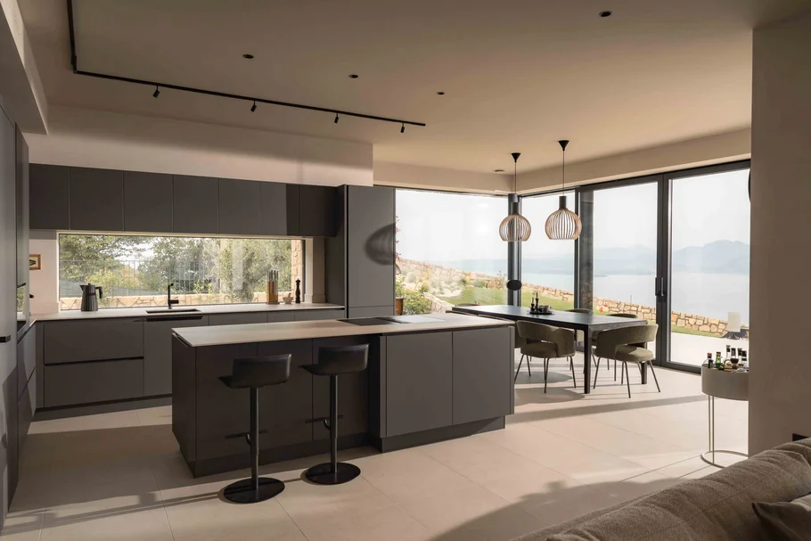 INTERIOS. Dein Interior-Design-Studio. Moderne Küche mit Kochinsel, Essbereich und Seeblick durch große Fenster