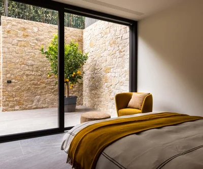 INTERIOS. Dein Interior-Design-Studio. Schlafzimmer mit gelbem Sessel und Blick auf Zitronenbaum hinter Glaswand