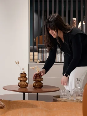 Hochwertige Designlösungen und Einrichtungskonzepte Frau arrangiert Dekorationsvase auf einem kleinen Tisch im Wohnzimmer