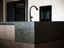 INTERIOS. Dein Interior-Design-Studio. Moderne Kücheninsel mit schwarzem Wasserhahn und dunkler Steinplatte