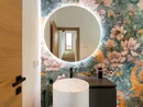 INTERIOS. Dein Interior-Design-Studio. Beleuchteter runder Spiegel über weißem Waschbecken und bunter Blumentapete