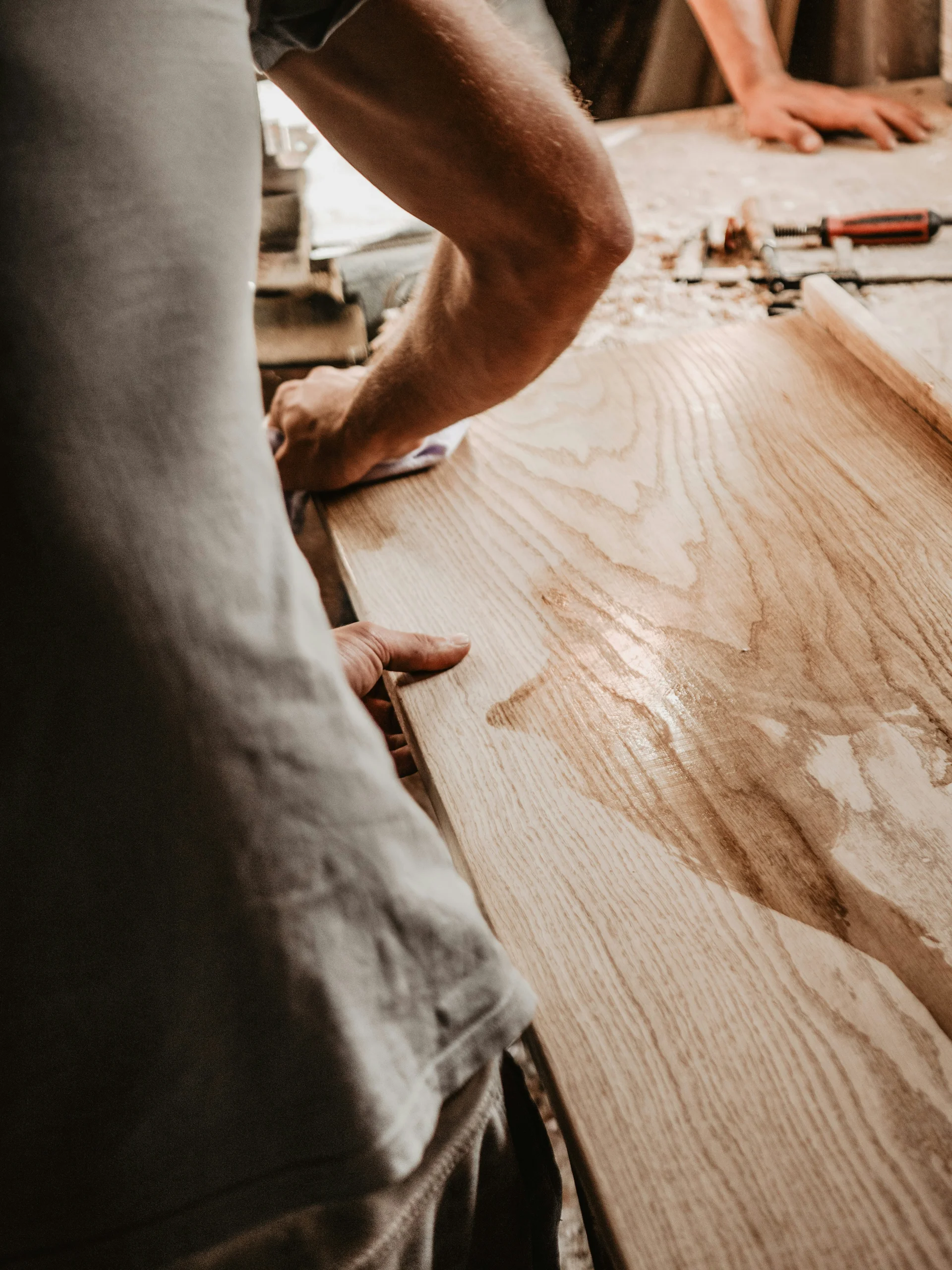 INTERIOS. Dein Interior-Design-Studio. Handwerker bearbeiten ein Holzbrett in einer Werkstatt