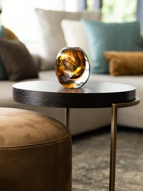 Home Staging und Möblierung Moderner Wohnzimmertisch mit braunem Glasaccessoire und Sofa im Hintergrund