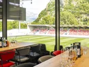 INTERIOS. Dein Interior-Design-Studio. Blick von einem VIP-Bereich auf ein Fußballstadion und grüne Berge