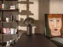 INTERIOS. Dein Interior-Design-Studio. Wohnzimmer mit Bücherregal, Tischlampe und Porträt einer Frau