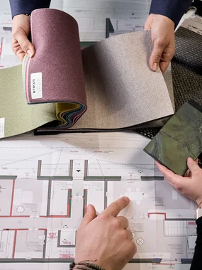 Technische Beratung und Machbarkeitsprüfung Personen vergleichen Stoffmuster auf einem architektonischen Bauplan