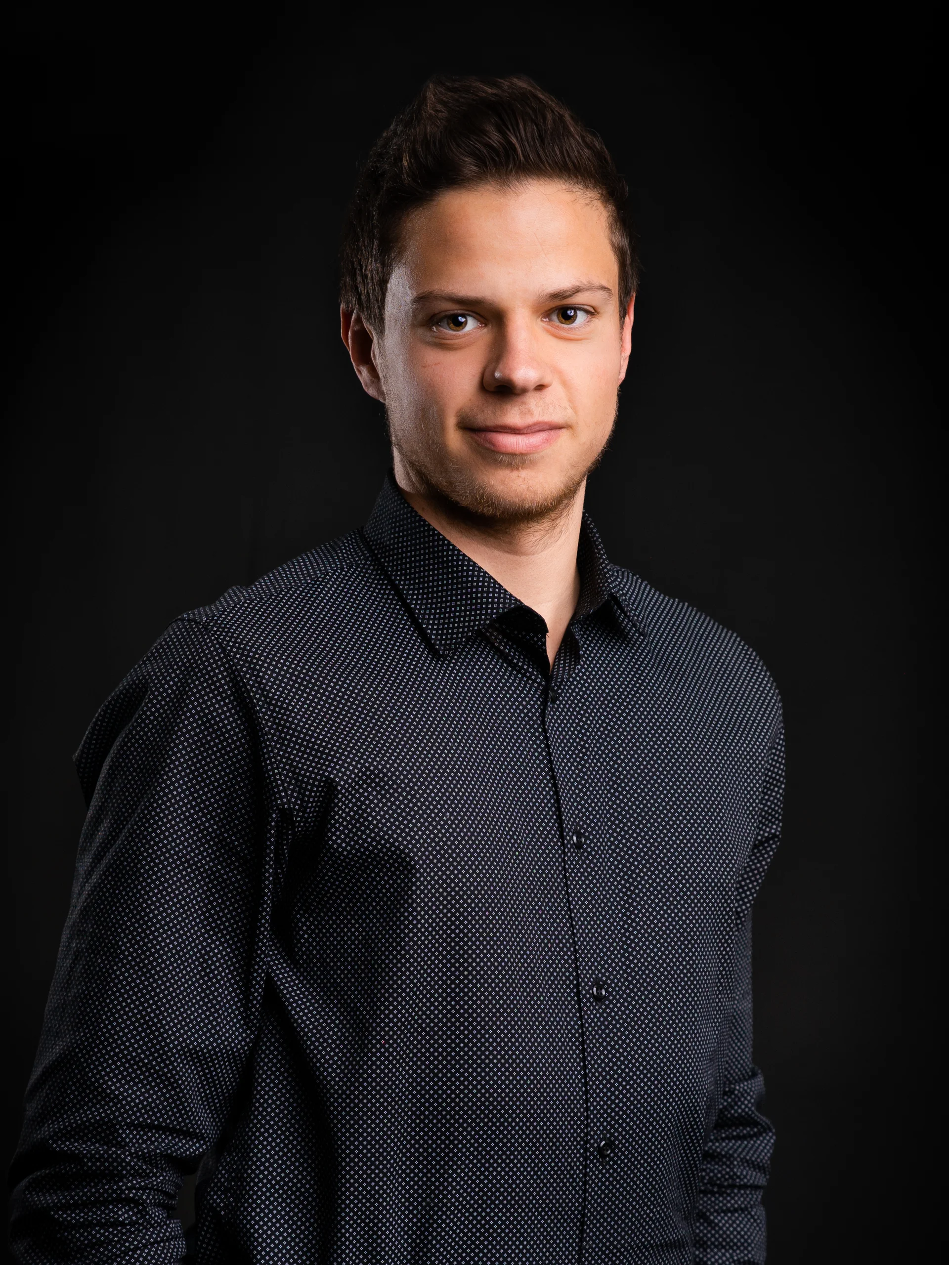 INTERIOS. Dein Interior-Design-Studio. Junger Mann in dunkelblauem Hemd vor schwarzem Hintergrund