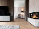 INTERIOS. Dein Interior-Design-Studio. Moderner Wohnraum mit Kamin, Fernseher und gemütlichem Sessel neben Stehlampe