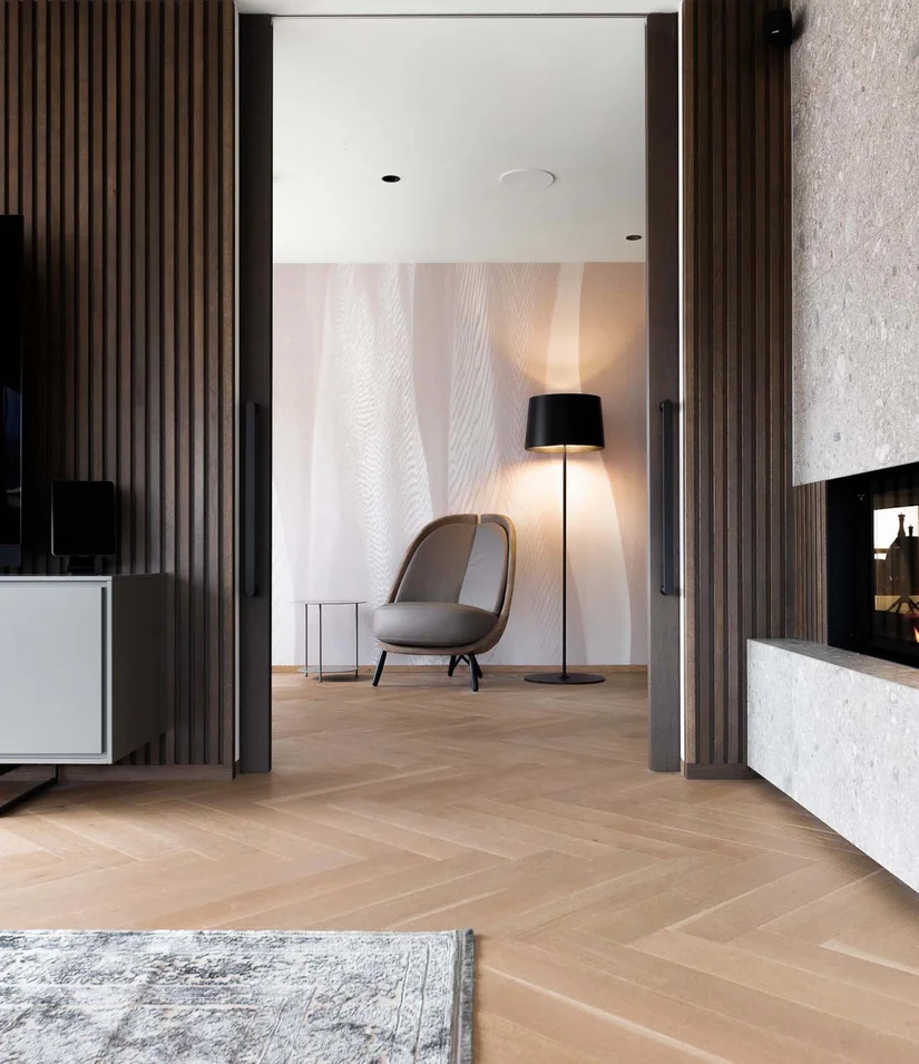 INTERIOS. Dein Interior-Design-Studio. Moderner Wohnraum mit Kamin, Fernseher und gemütlichem Sessel neben Stehlampe