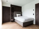 INTERIOS. Dein Interior-Design-Studio. Modernes Schlafzimmer mit Einzelbett, dunklen Holztüren und hellem Parkettboden