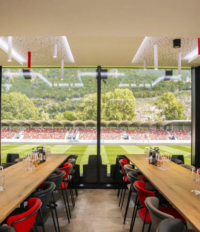 INTERIOS. Dein Interior-Design-Studio. Blick auf ein Fußballstadion von einem Innenraum mit Tischen und Stühlen