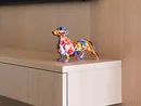 INTERIOS. Dein Interior-Design-Studio. Bunte Dackel-Statue auf hellem Holzregal unter einem Fernseher