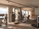 INTERIOS. Dein Interior-Design-Studio. Heller Fitnessraum mit Trainingsgeräten und großen Fenstern mit Bergblick
