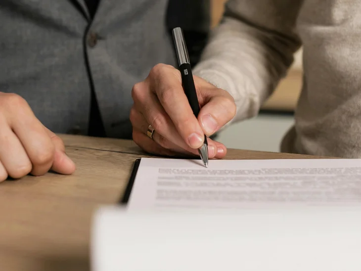 INTERIOS. Dein Interior-Design-Studio. Person unterschreibt Dokument während andere Person danebensteht