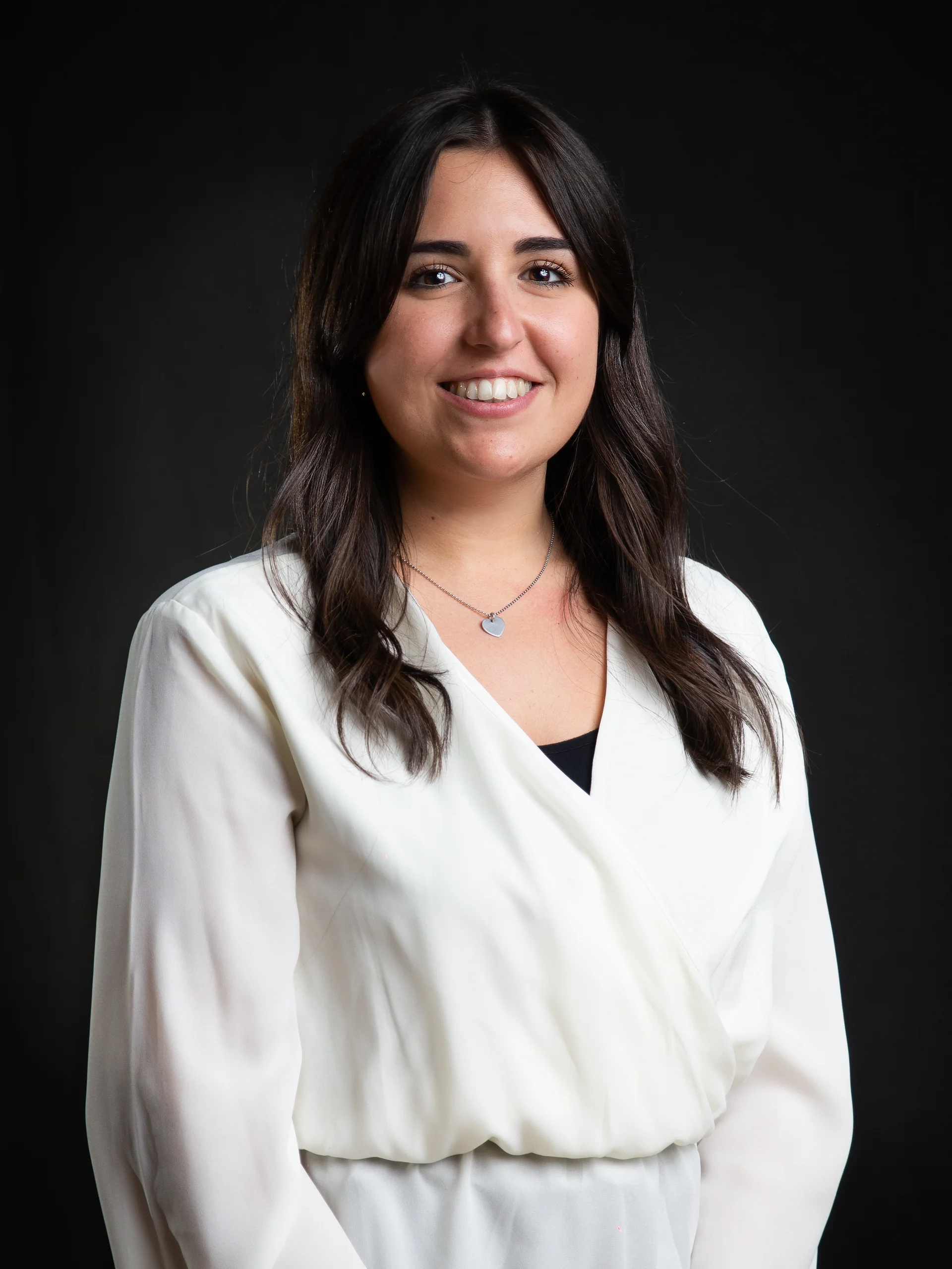 INTERIOS. Dein Interior-Design-Studio. Porträt einer lächelnden Frau mit weißer Bluse vor schwarzem Hintergrund