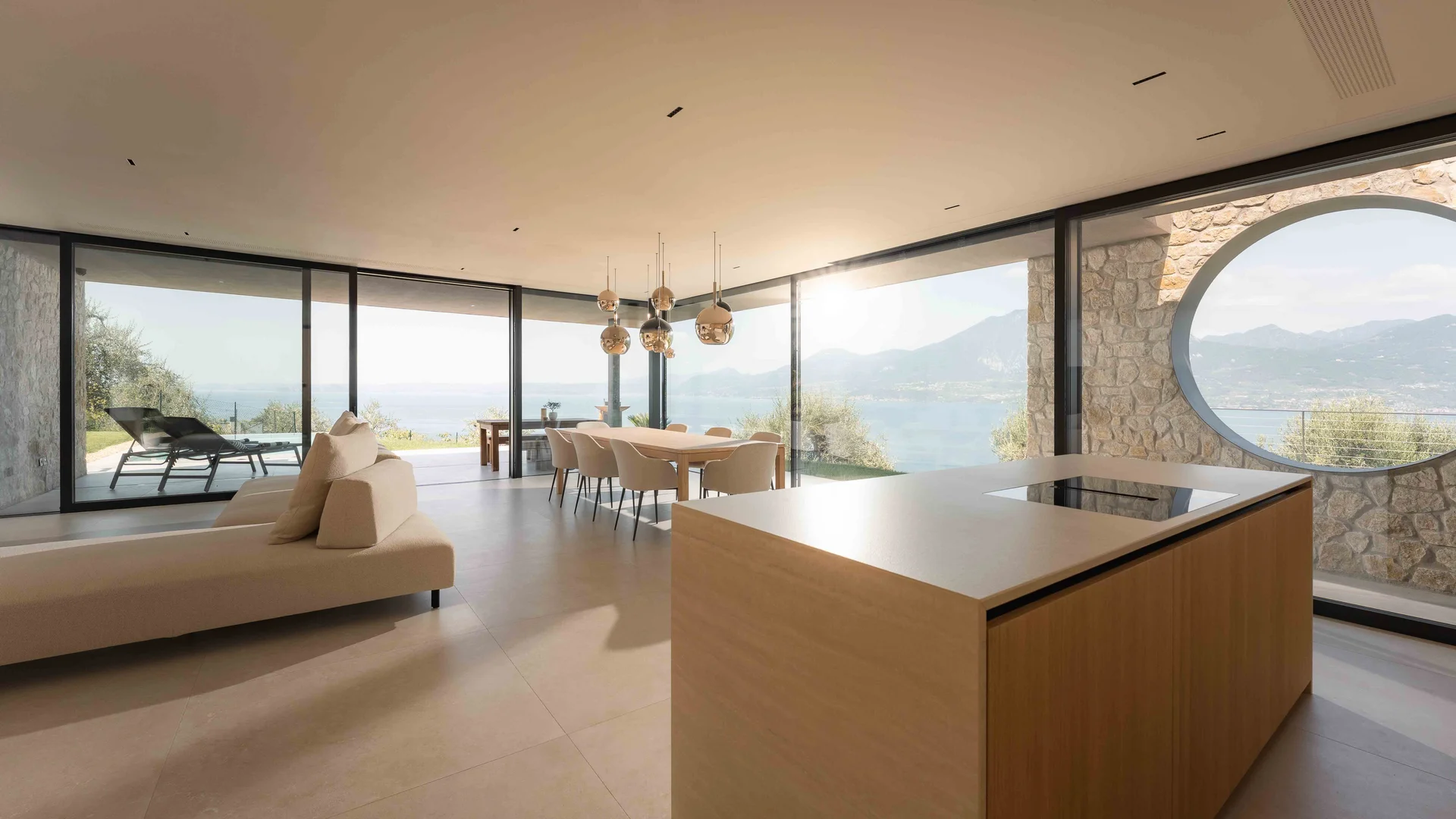 INTERIOS. Dein Interior-Design-Studio. Modernes Wohnzimmer mit Küche, Esstisch und Panoramablick auf See und Berge