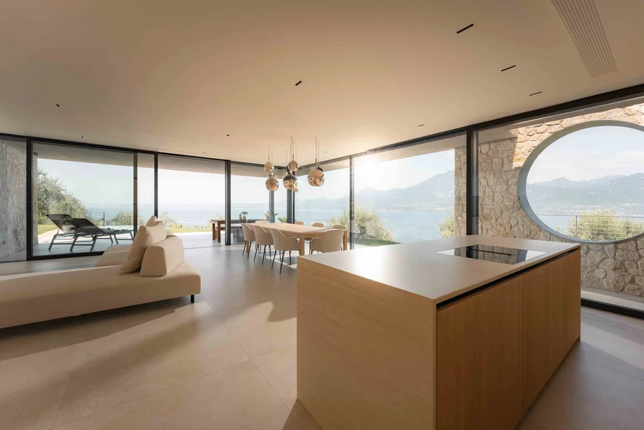 INTERIOS. Dein Interior-Design-Studio. Modernes Wohnzimmer mit Küche, Esstisch und Panoramablick auf See und Berge