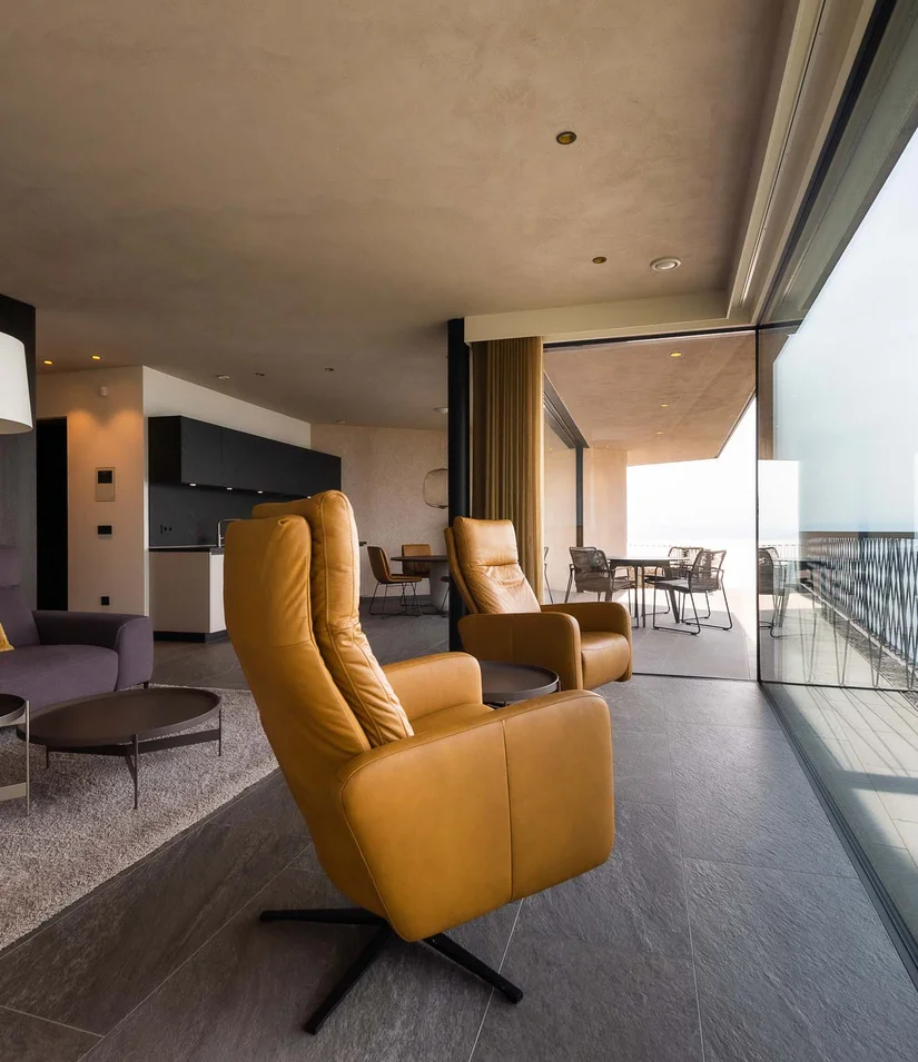 INTERIOS. Dein Interior-Design-Studio. Modernes Wohnzimmer mit Ledersesseln und Meerblick durch Panoramafenster