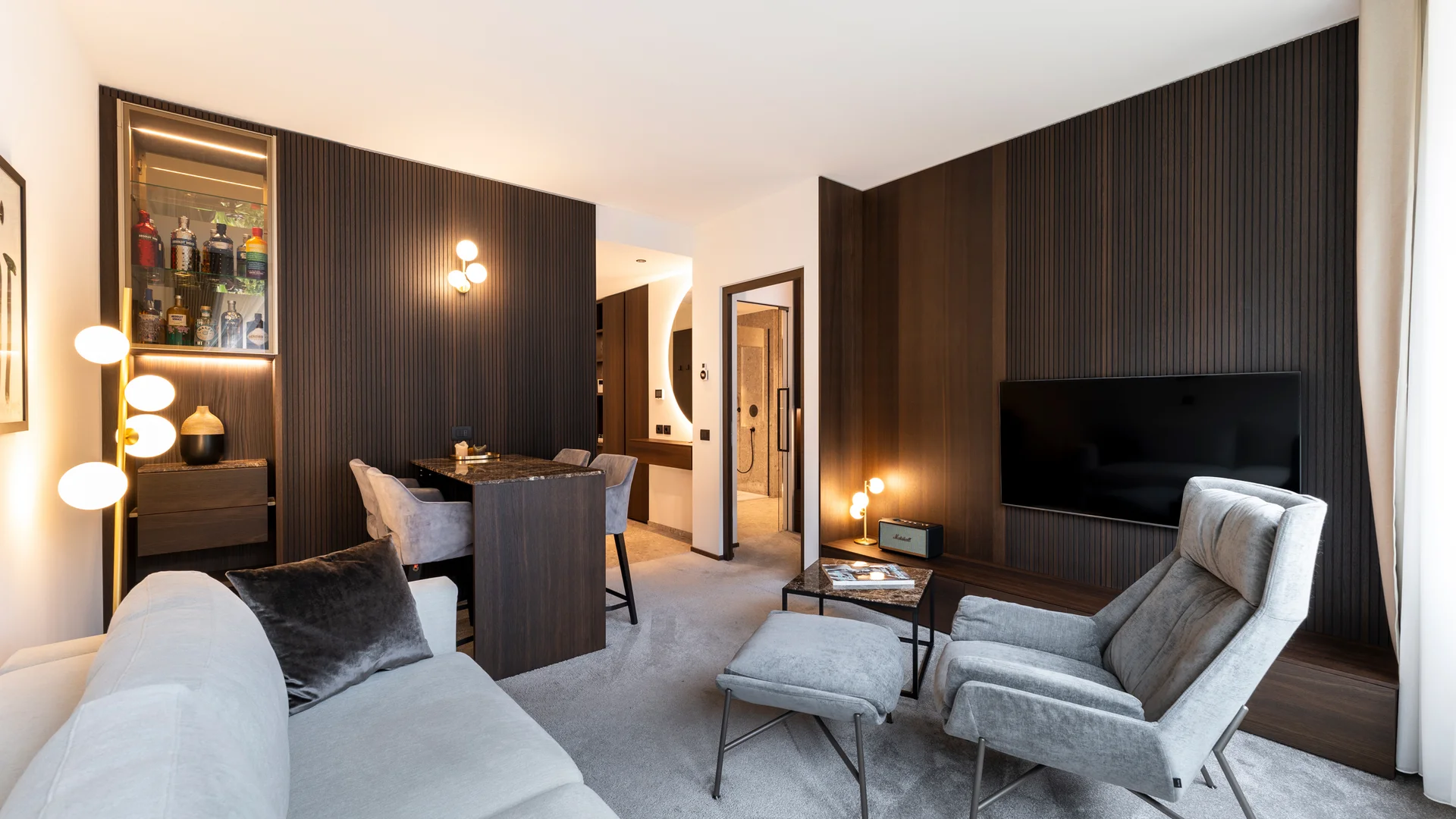 INTERIOS. Dein Interior-Design-Studio. Modernes Wohnzimmer mit grauem Sofa, Sessel und dunklen Holzwänden