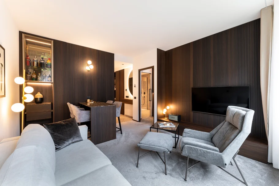 INTERIOS. Dein Interior-Design-Studio. Modernes Wohnzimmer mit grauem Sofa, Sessel und dunklen Holzwänden