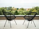 INTERIOS. Dein Interior-Design-Studio. Zwei schwarze Stühle auf Balkon mit Blick auf grüne Bäume und Stadt im Hintergrund