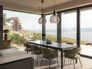 INTERIOS. Dein Interior-Design-Studio. Heller Essbereich mit Esstisch, Stühlen und Blick auf See und Berge durch große Fenster