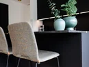 INTERIOS. Dein Interior-Design-Studio. Zwei gepolsterte Stühle an einer schwarzen Kücheninsel mit Dekopflanzen