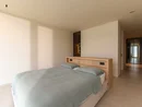 INTERIOS. Dein Interior-Design-Studio. Helles Schlafzimmer mit Doppelbett, grauer Bettdecke und angrenzendem Flur