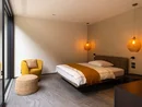 INTERIOS. Dein Interior-Design-Studio. Modernes Schlafzimmer mit gelbem Sessel, Bett und warmen Hängelampen