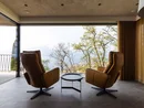 INTERIOS. Dein Interior-Design-Studio. Zwei Ledersessel mit Blick auf eine Terrasse und Landschaft mit Bäumen und Wasser